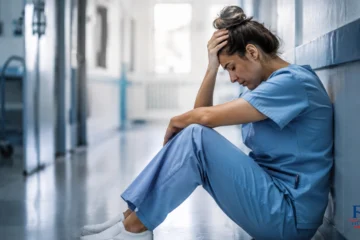 operatrice sanitaria stressata seduta in corridoio ospedaliero durante un momento di forte disagio lavorativo